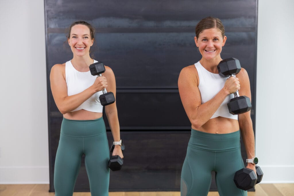 two women performing alternating cross body bicep curls in an arm workout