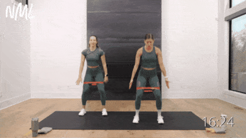 two women performing squats with a resistance band