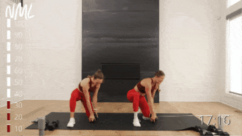 two women performing a half kneeling dumbbell pick up and toss