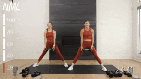 two women performing a lateral squat with a front raise as part of dumbbell snatch workout