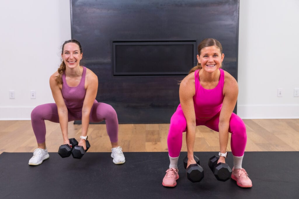 two women performing a low squat hold as part of full body dumbbell workout