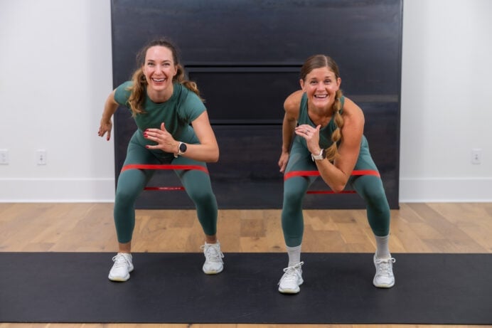 two women performing a staggered squat exercise with resistance bands