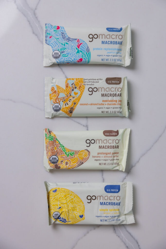 Four GoMarco protein bars with flavors including peanut butter, coconut, almond butter and chocolate chip, banana and almond butter, and lemon.  