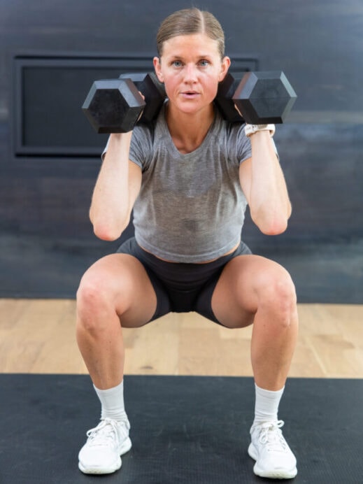 woman performing a squat hold with dumbbells front racked in a leg workout