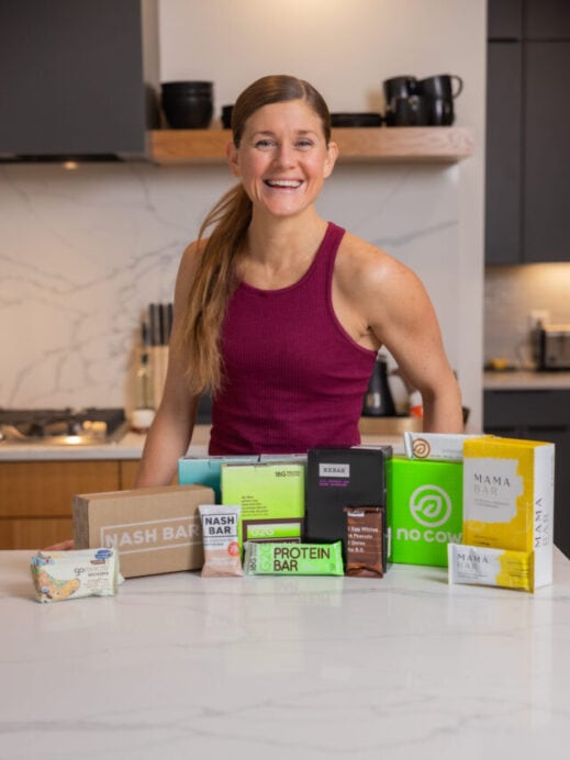 Woman in her kitchen with brands of protein bars; no cow, g2g bars, rx bars, gomarco bars, mama bars and nash bars.