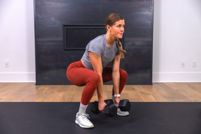 woman performing a glute biased squat with dumbbells in a glute workout