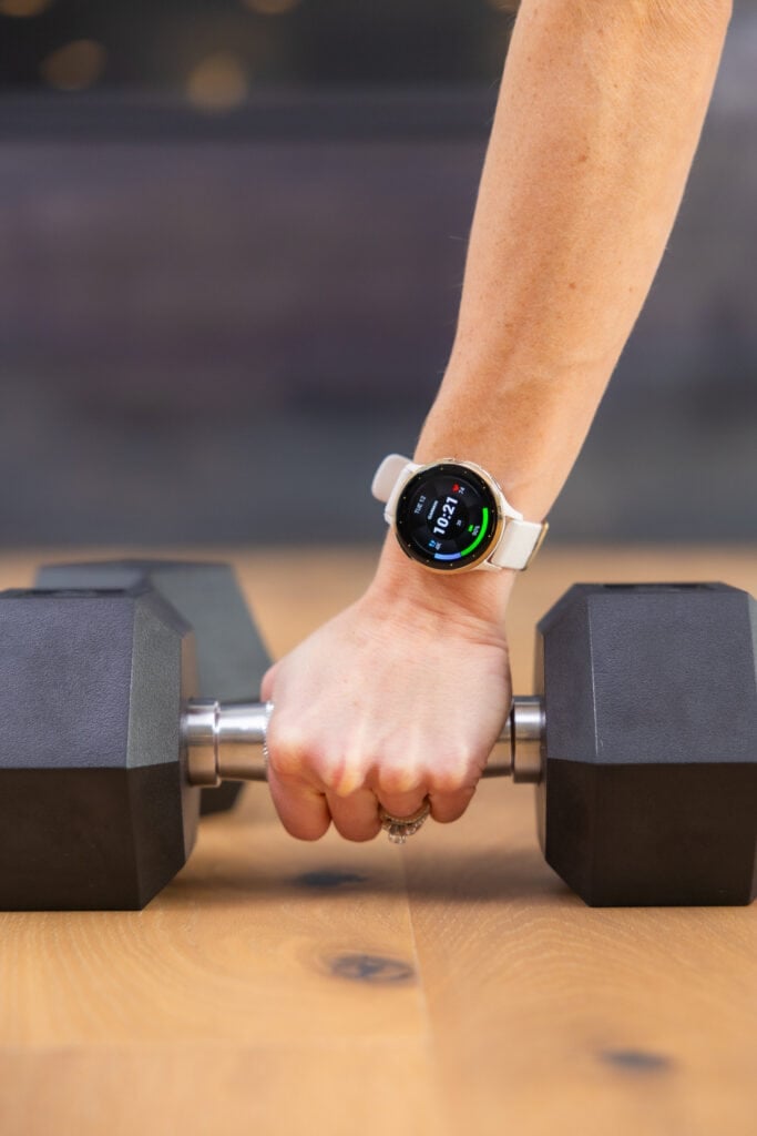 Women grabbing a dumbbell off the floor and wearing a Garmin Venu 3 Watch.