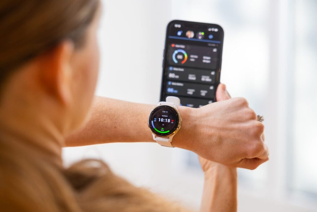 Women wearing garmin venu 3 on her left wrist and holding her phone with the garmin app open in her right hand. 