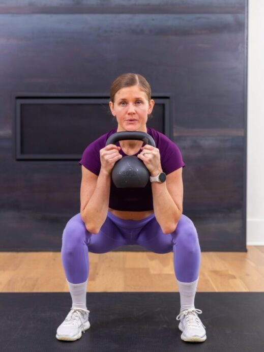 woman holding kettlebell at her chest in a low squat position