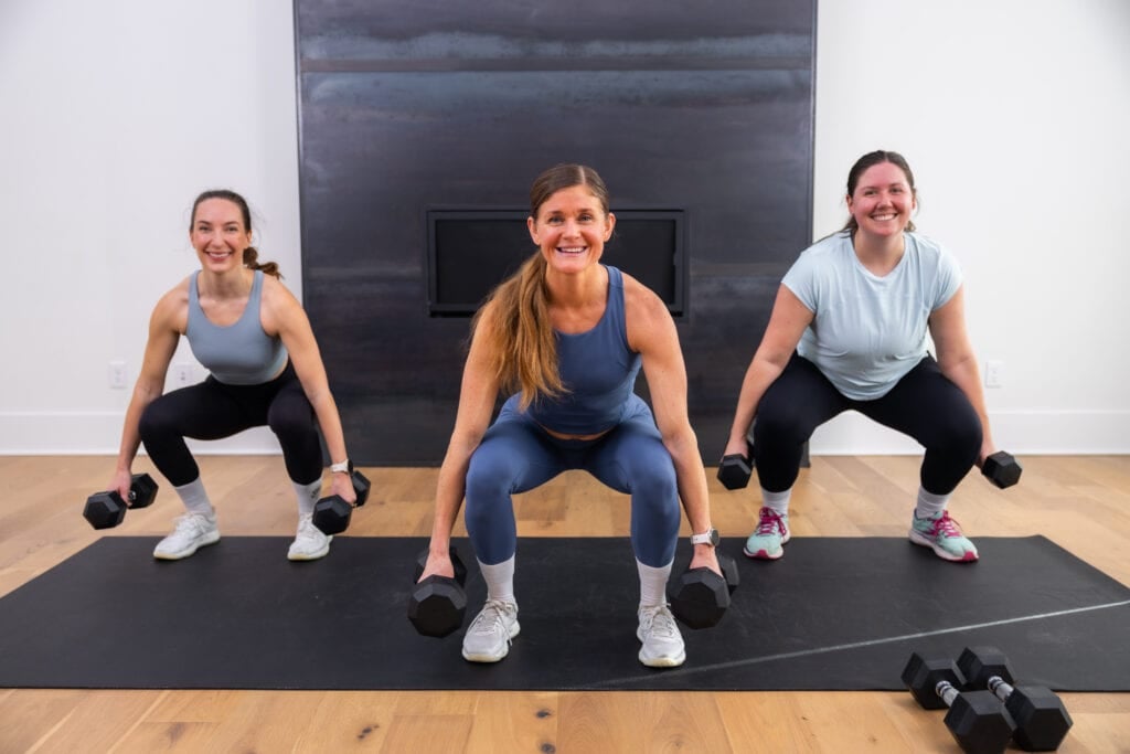 three women performing a squat as part of dumbbell workout routine