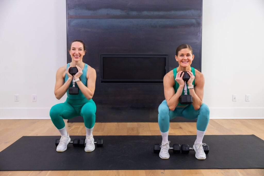 two women performing a heels up squat variation with dumbbells to target quads