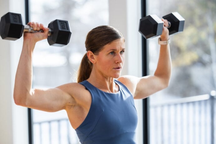 woman performing dumbbell shoulder press as part of dumbbell workout routine