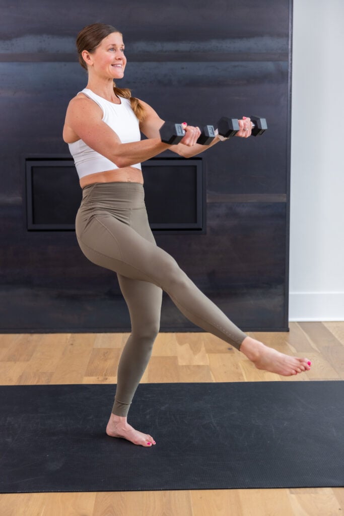 woman performing a single leg front lift and dumbbell press out in a barre pilates class at home