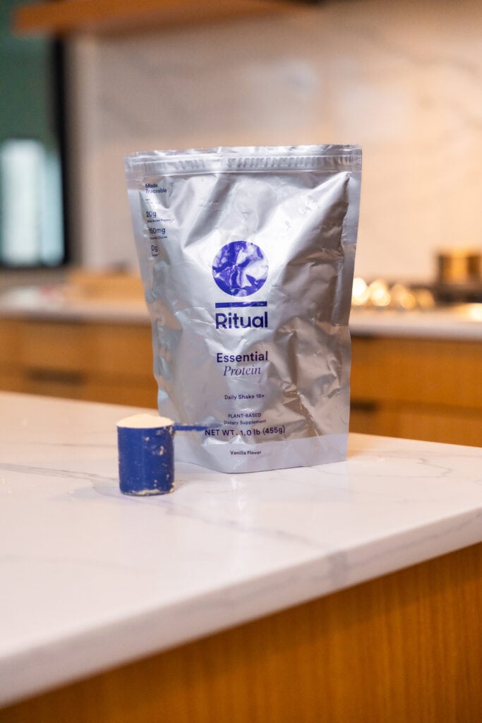 ritual essential protein powder on countertop with a scoop of vanilla protein as part of best protein powder