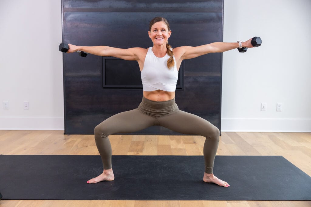 Woman performing a plie with a shoulder raise as part of full body pilates barre workout
