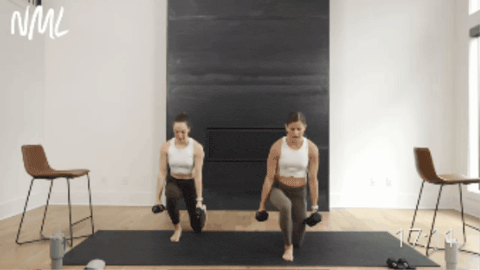 two women performing a reverse lunge, balance hold and bicep press out as part of pilates barre class