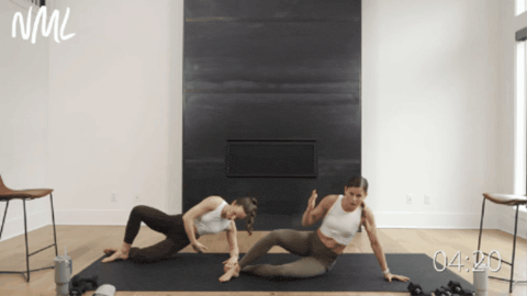 two women performing a side plank with a reach as part of pilates barre workout