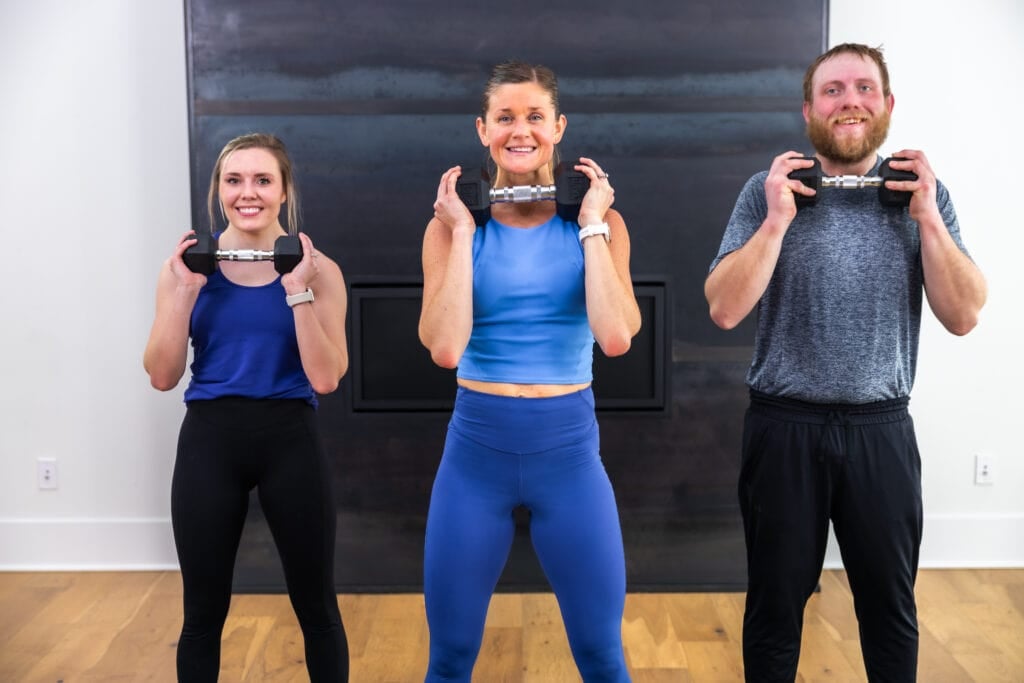 three people performing a dumbbell shoulder press as part of total body workout