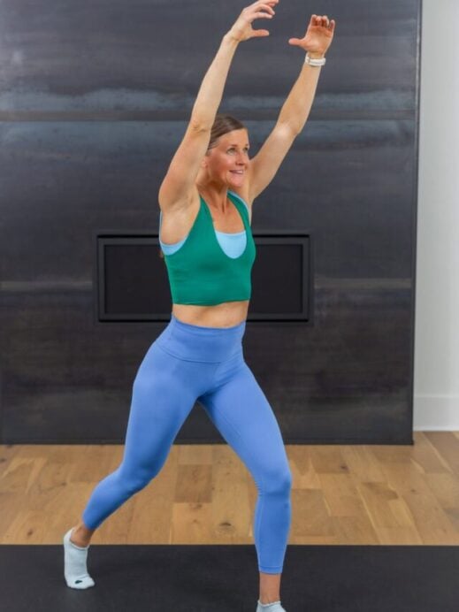 woman with her arms raised overhead preparing to perform a straight leg kick in a quick ab workout