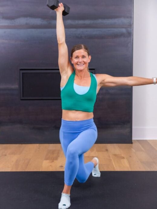 woman performing a reverse lunge and overhead press with light weights in a barre pilates workout