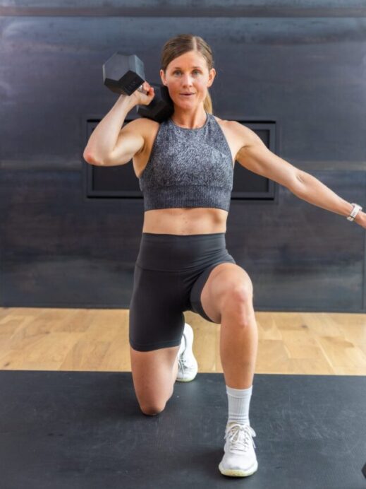 woman holding a reverse lunge and a dumbbell front racked on one shoulder in a full body workout