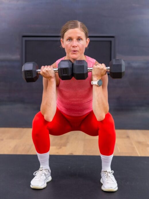 woman holding a low squat with dumbbells in a front racked position in a full body workout