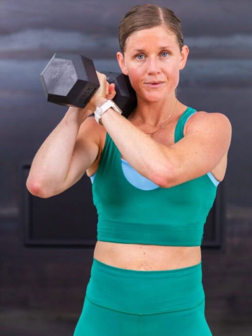 woman holding one dumbbell front racked at her shoulder in a full body workout