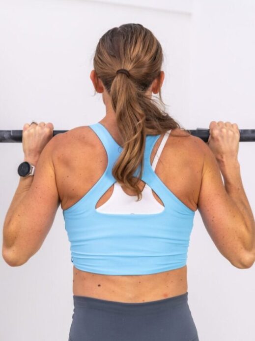 woman holding the top of a pull up as part of an assisted pull up tutorial