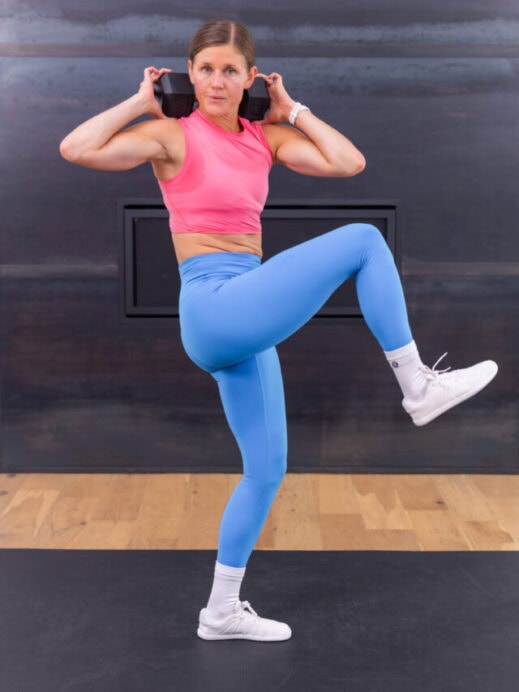 woman holding a dumbbell across her back for a good morning and drop step crossbody crunch