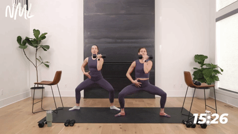 two women performing a second position squat and single arm Arnold press in a barre workout