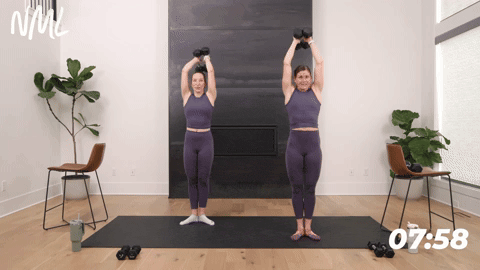 two women holding tree pose and performing overhead triceps in a barre workout
