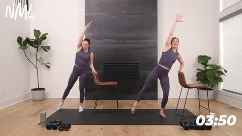 two women performing a standing oblique crunch in a barre workout