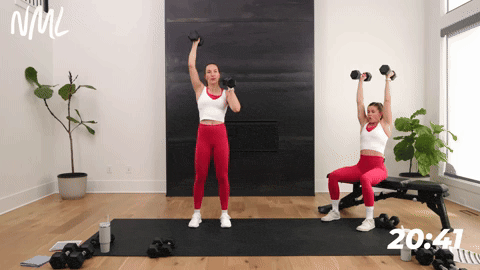 two women performing an alternating shoulder press with dumbbells in a chest shoulders and triceps workout