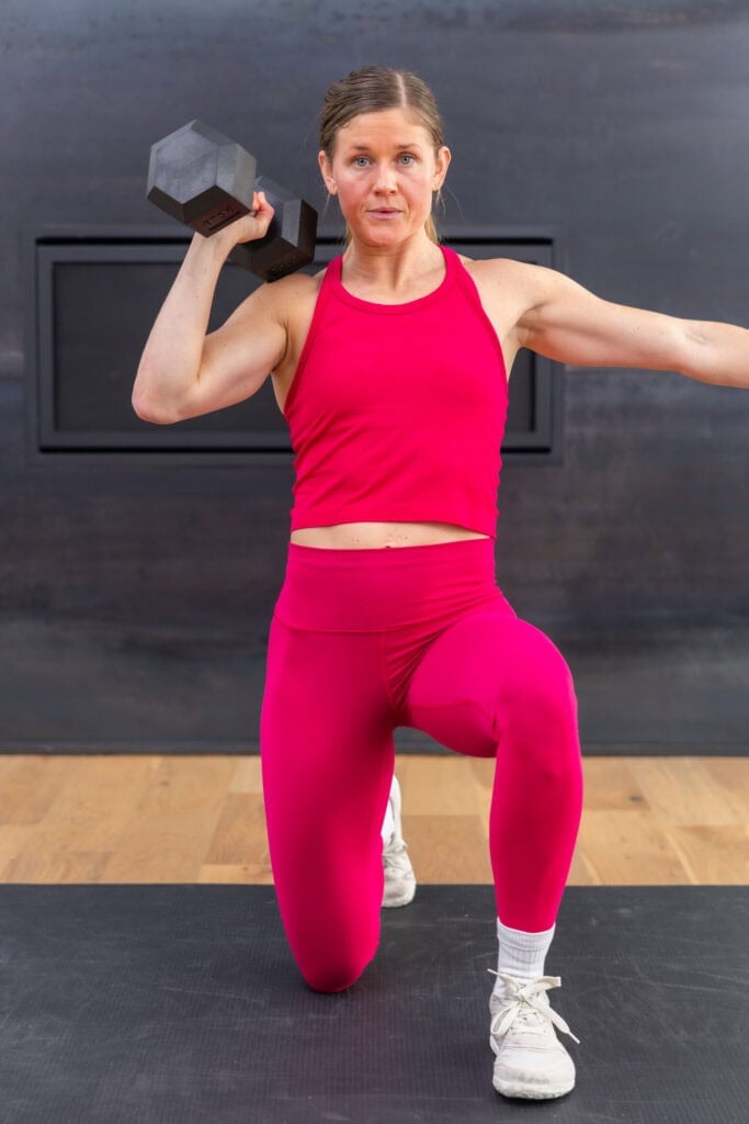 woman performing a kneeling overhead press in a strength workout for runners