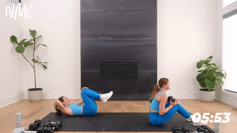 one women performing a dumbbell sit up to stand up with one dumbbell. one women performing bodyweight deadbugs. 