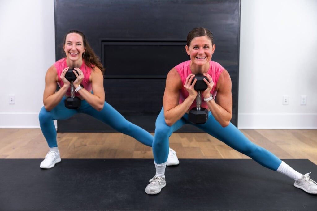 two women performing a lateral squat with a dumbbell in a full body hiit workout