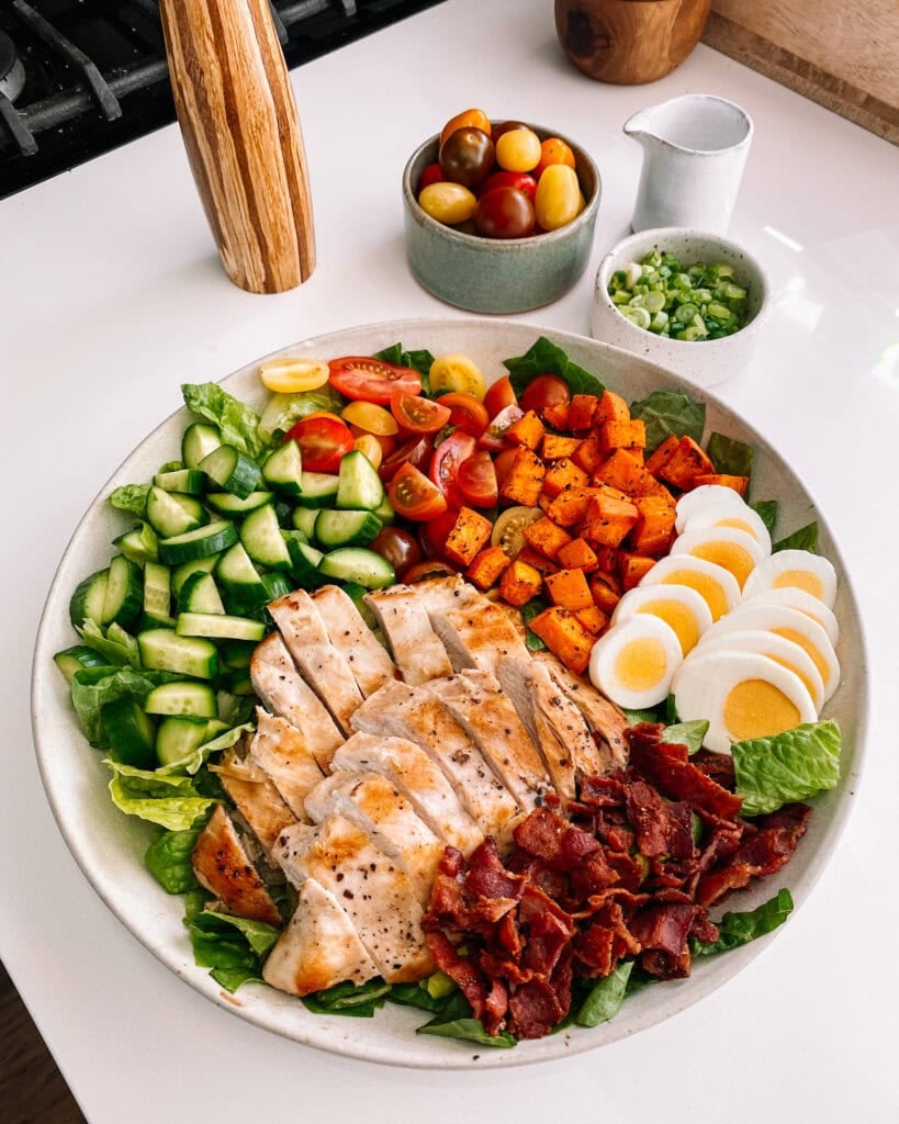 High protein cobb salad with chicken, hard boil eggs, sweet potatoes, cucumber, tomatoes, and bacon.