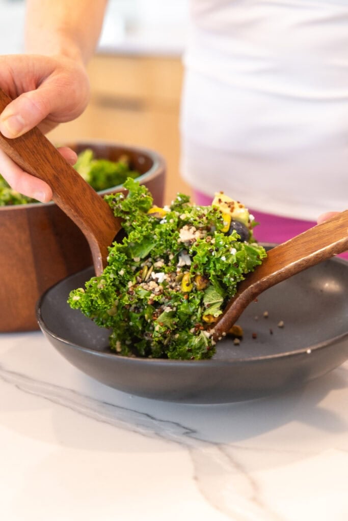 A person is stirring a bowl of a kale quinoa salad.
