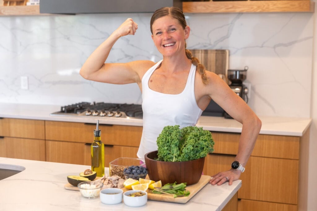Women making a high protein salad recipe with kale, chicken, blueberries, quinoa, olive oil and avocado. 