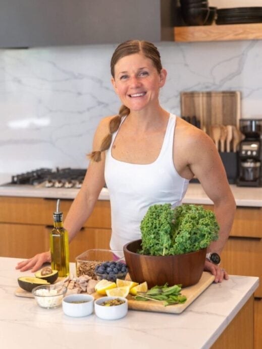 Women with salad ingredients including fresh kale, pumpkin seeds, feta cheese, mint, lemon juice, blueberry, chicken, avocado, quinoa and olive oil.