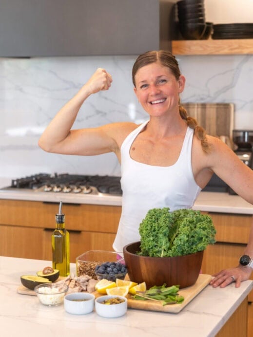 Women with salad ingredients including fresh kale, pumpkin seeds, feta cheese, mint, lemon juice, blueberry, chicken, avocado, quinoa and olive oil.