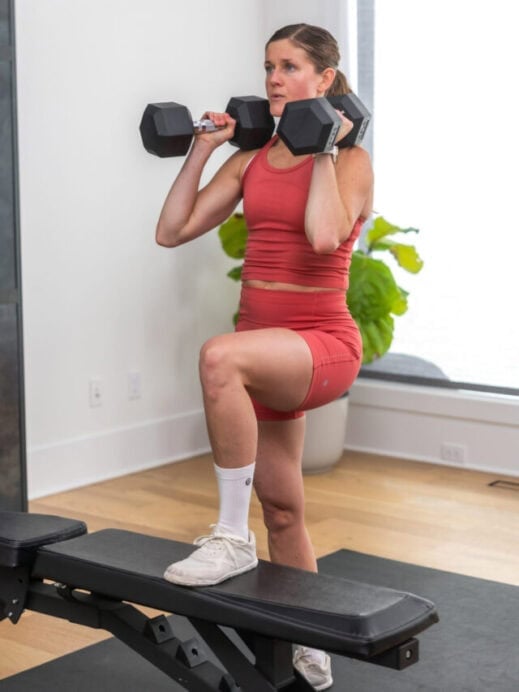 woman performing a dumbbell clean and knee drive onto a bench in a glute and hamstring workout