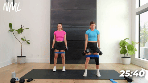 two women performing banded dumbbell squats in a leg workout