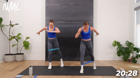 two women performing a staggered squat and rear foot tap back in a booty band workout