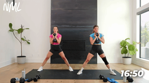 two women performing lateral squats with dumbbells in a leg workout