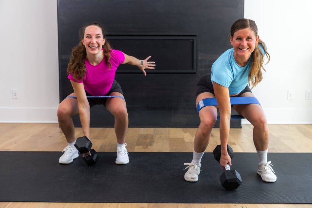 two women performing a banded squat jack in a leg workout at home