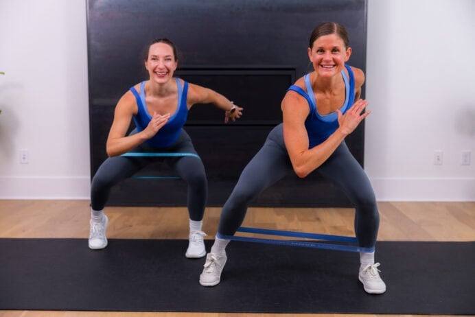 two women performing banded side step squats in a booty band workout