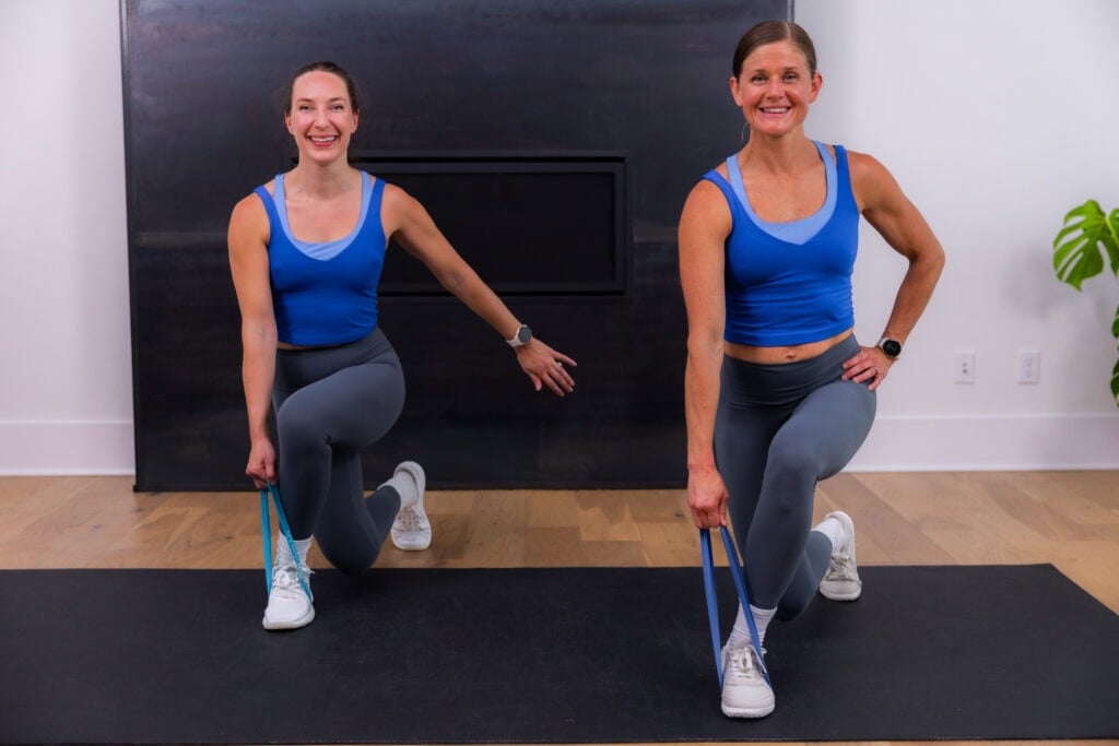 two women performing curtsy lunges with a resistance band in a booty band workout