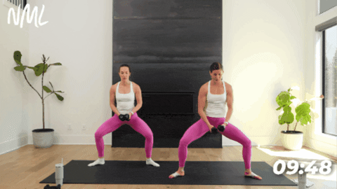 women demonstrating a plie squat with a lateral raise as part of home barre workout