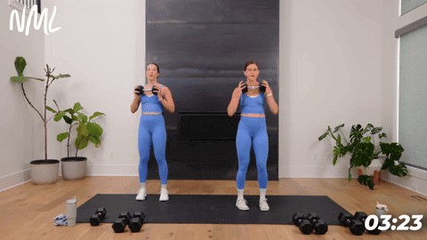 two women performing a standing chest press with a dumbbell in a 20 minute home workout